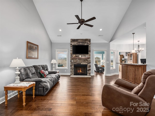 living room featuring ceiling fan with notable chandelier, a wealth of natural light, a stone fireplace, and dark hardwood / wood-style flooring