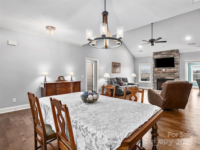 dining space with dark wood-type flooring, lofted ceiling, a stone fireplace, and ceiling fan with notable chandelier