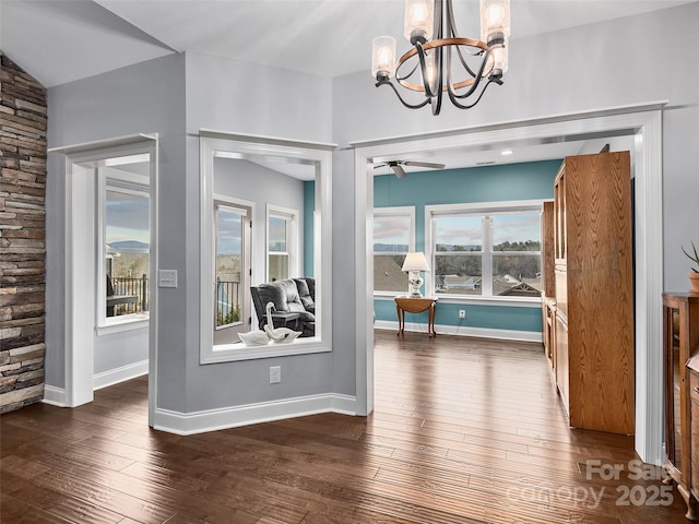 unfurnished dining area with ceiling fan with notable chandelier, a wealth of natural light, and dark hardwood / wood-style flooring