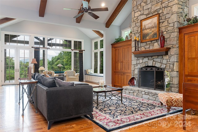 living room with light hardwood / wood-style floors, beam ceiling, high vaulted ceiling, a stone fireplace, and ceiling fan