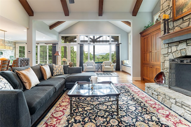 living room with vaulted ceiling with beams, a stone fireplace, and light hardwood / wood-style floors