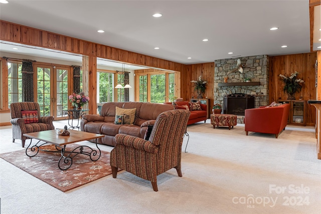 living room with light colored carpet, a stone fireplace, wooden walls, and plenty of natural light