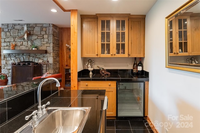 bar featuring a stone fireplace, beverage cooler, dark tile patterned flooring, and sink