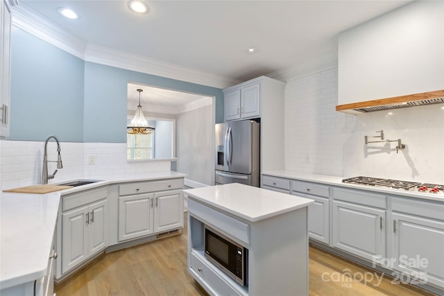 kitchen with appliances with stainless steel finishes, white cabinetry, sink, hanging light fixtures, and light wood-type flooring