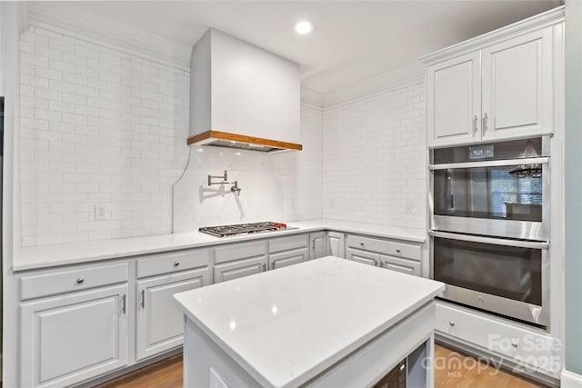 kitchen with backsplash, custom range hood, white cabinets, and appliances with stainless steel finishes