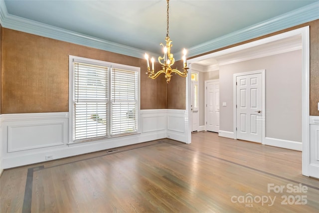 unfurnished dining area with hardwood / wood-style flooring, crown molding, and an inviting chandelier