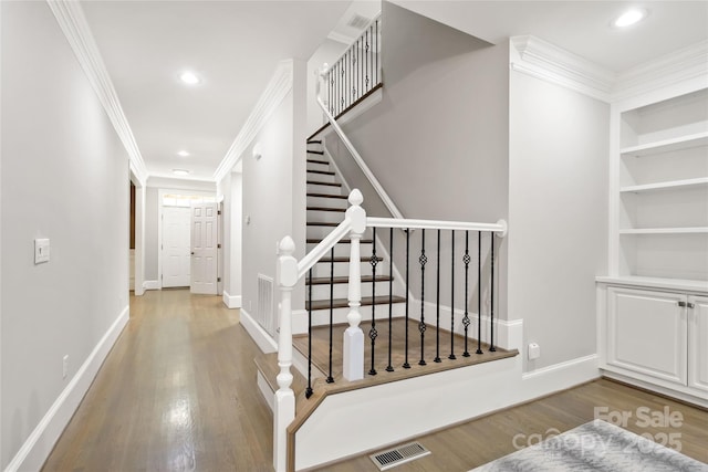 stairway with wood-type flooring, crown molding, and built in shelves