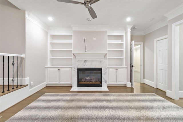 unfurnished living room featuring wood-type flooring, ornamental molding, ceiling fan, a high end fireplace, and built in shelves