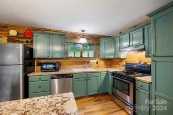 kitchen featuring light stone countertops, hanging light fixtures, stainless steel appliances, and light wood-type flooring