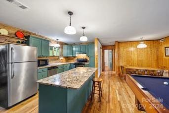 kitchen with appliances with stainless steel finishes, pool table, a center island, pendant lighting, and light hardwood / wood-style flooring