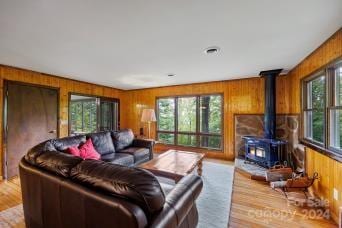 living room with light hardwood / wood-style floors, a wood stove, a wealth of natural light, and wooden walls