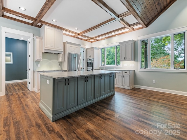 kitchen featuring light stone countertops, stainless steel fridge, coffered ceiling, gray cabinets, and an island with sink