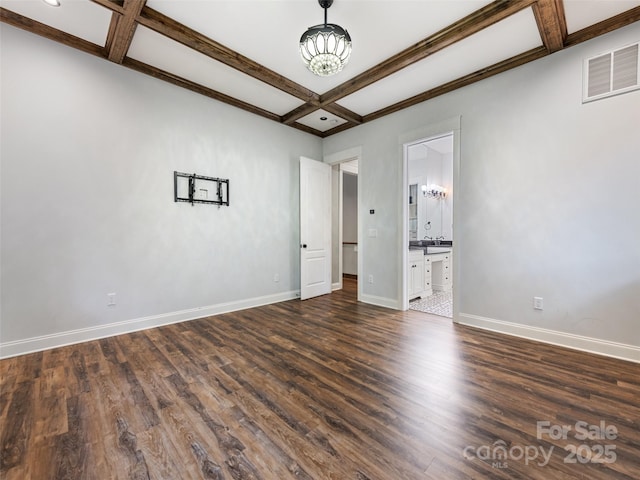 unfurnished bedroom featuring beam ceiling, ensuite bath, dark wood-type flooring, and coffered ceiling