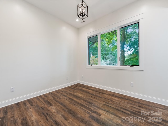 empty room with a chandelier and dark wood-type flooring