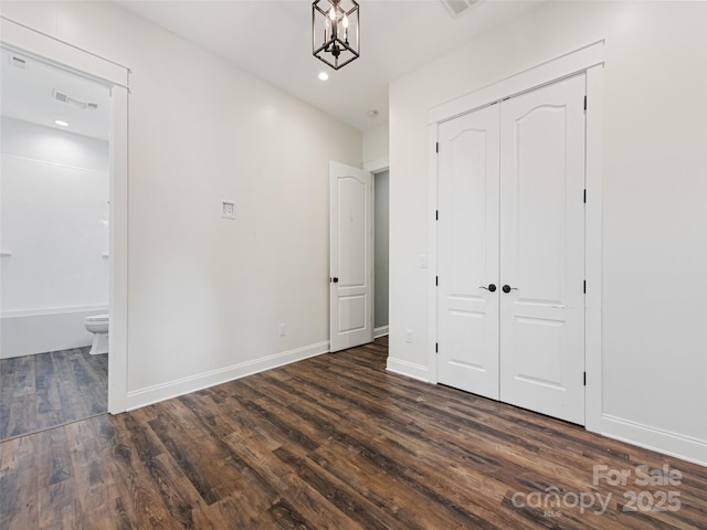 unfurnished bedroom featuring dark hardwood / wood-style floors, ensuite bath, a closet, and a notable chandelier