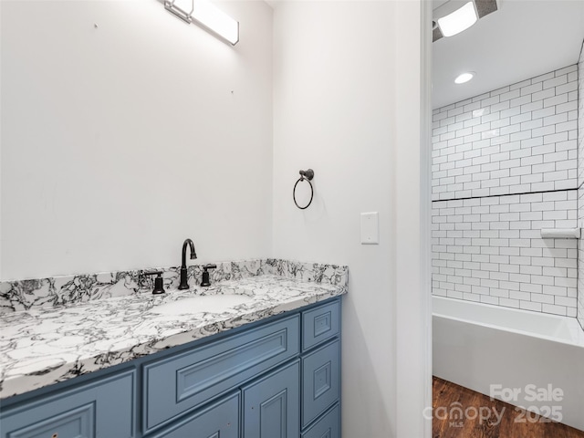 bathroom with hardwood / wood-style flooring, vanity, and tiled shower / bath