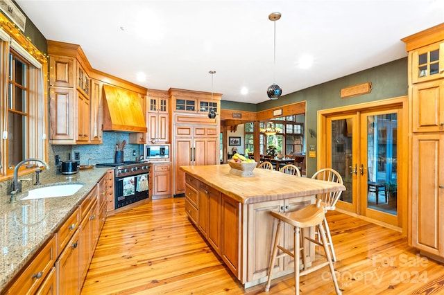 kitchen featuring light wood-type flooring, a center island, sink, custom exhaust hood, and appliances with stainless steel finishes