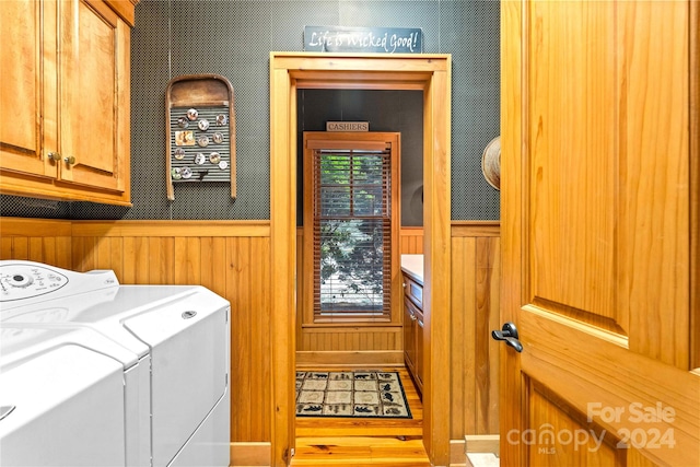 laundry area with wood-type flooring, wood walls, washing machine and clothes dryer, and cabinets