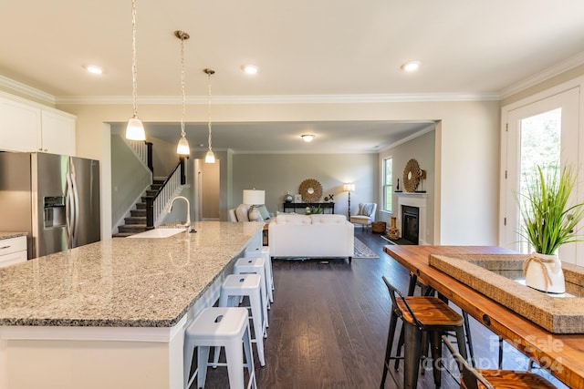 kitchen featuring a large island with sink, stainless steel fridge with ice dispenser, hanging light fixtures, and dark hardwood / wood-style floors