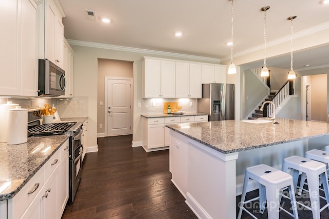 kitchen featuring appliances with stainless steel finishes, dark hardwood / wood-style floors, a kitchen island with sink, and decorative light fixtures