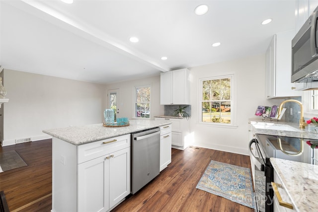 kitchen with light stone counters, a center island, dark wood-type flooring, white cabinets, and stainless steel appliances