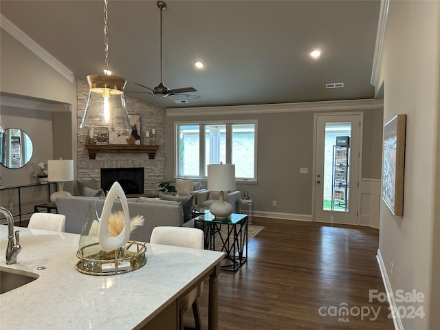 living room with sink, a stone fireplace, dark hardwood / wood-style flooring, ceiling fan, and crown molding