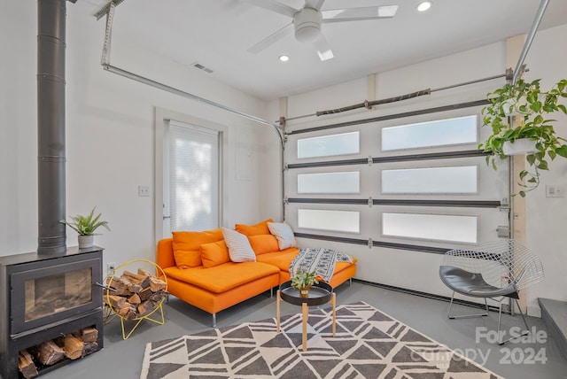 living area featuring ceiling fan, concrete floors, and a wood stove