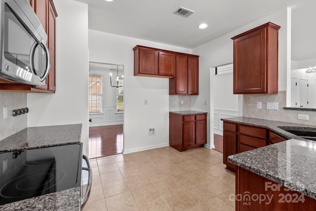 kitchen with range, pendant lighting, decorative backsplash, dark stone countertops, and an inviting chandelier