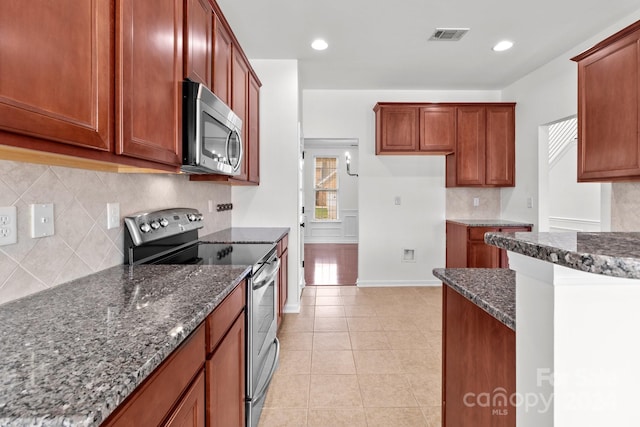 kitchen featuring decorative backsplash, dark stone countertops, appliances with stainless steel finishes, and light tile patterned floors