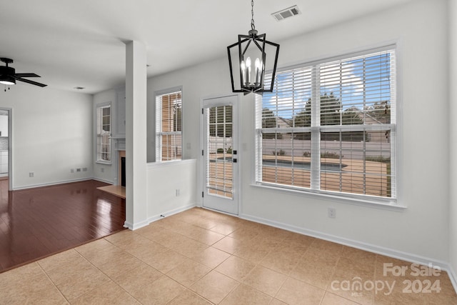 unfurnished dining area with ceiling fan with notable chandelier, light hardwood / wood-style floors, and plenty of natural light