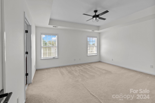 empty room with light carpet, a raised ceiling, and ceiling fan