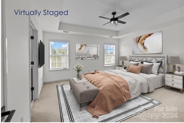 carpeted bedroom featuring a tray ceiling, multiple windows, and ceiling fan