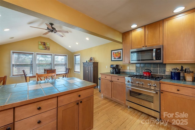 kitchen with appliances with stainless steel finishes, backsplash, ceiling fan, tile countertops, and light hardwood / wood-style flooring