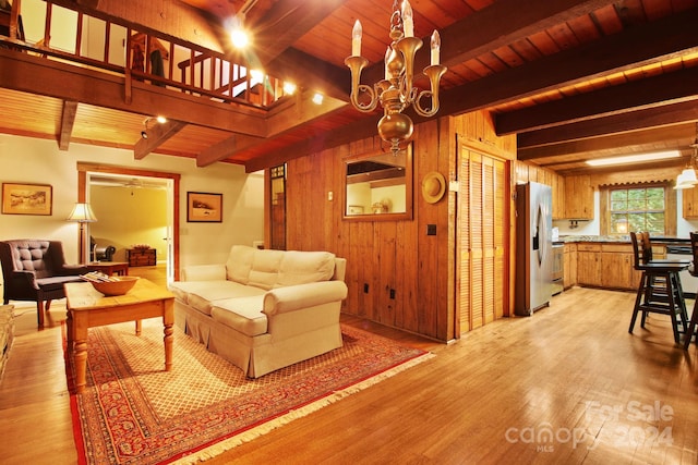 living room with beamed ceiling, light hardwood / wood-style floors, a chandelier, and wooden walls