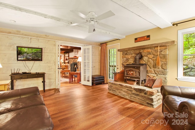 living room featuring wood-type flooring, a wood stove, plenty of natural light, and ceiling fan