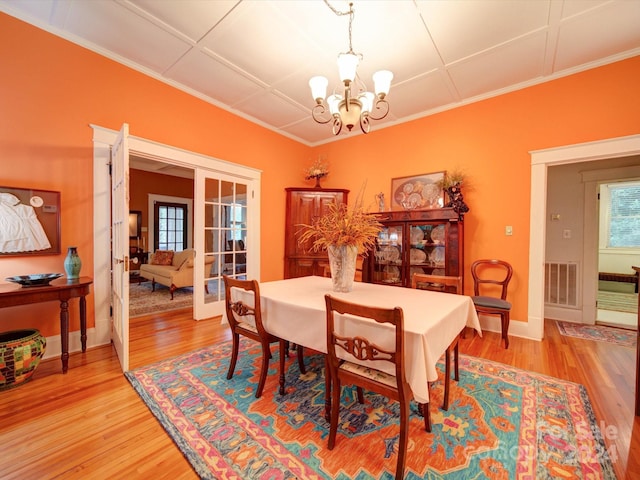 dining space featuring a notable chandelier, hardwood / wood-style flooring, french doors, and crown molding