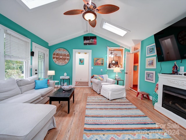 living room with vaulted ceiling with skylight, light hardwood / wood-style floors, and ceiling fan