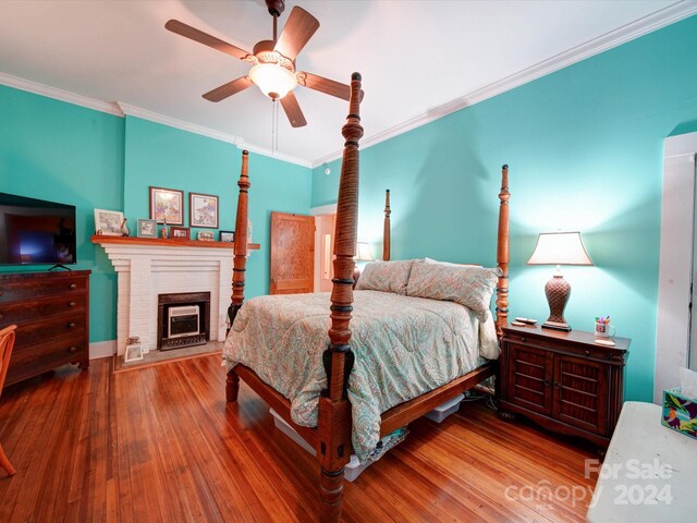 bedroom with crown molding, ceiling fan, a brick fireplace, and hardwood / wood-style flooring