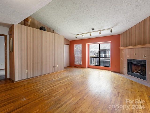 unfurnished living room with a fireplace, light wood-type flooring, a textured ceiling, lofted ceiling, and wooden walls