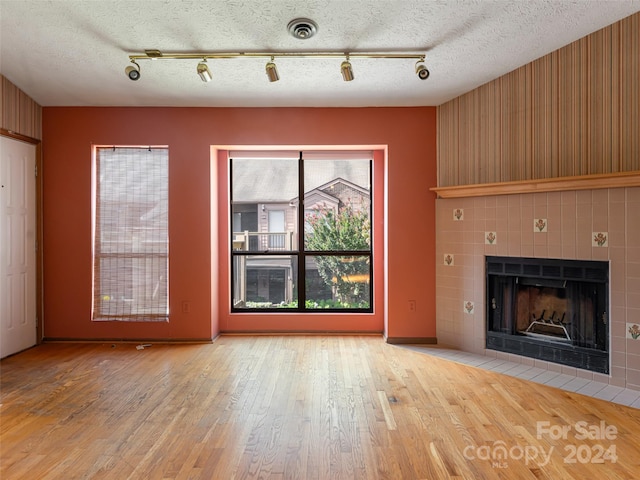 unfurnished living room featuring a textured ceiling, a tile fireplace, wood walls, and wood-type flooring