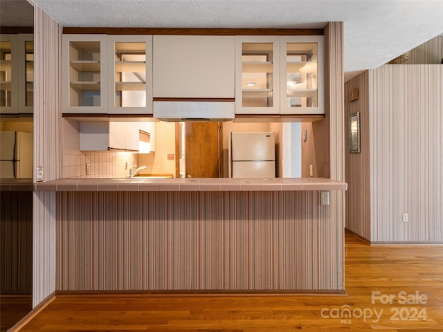 kitchen featuring white refrigerator, light wood-type flooring, kitchen peninsula, and tasteful backsplash