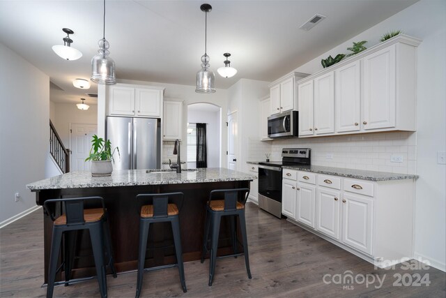 kitchen with appliances with stainless steel finishes, decorative light fixtures, a kitchen island with sink, and white cabinets