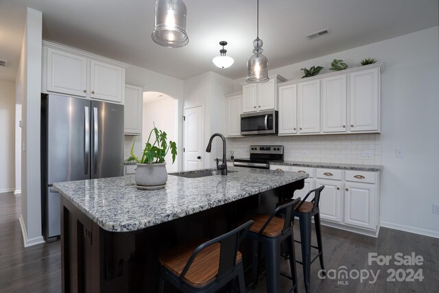 kitchen featuring appliances with stainless steel finishes, a center island with sink, backsplash, and white cabinetry