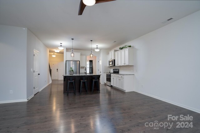 kitchen with pendant lighting, dark wood-type flooring, a kitchen island with sink, white cabinets, and stainless steel appliances