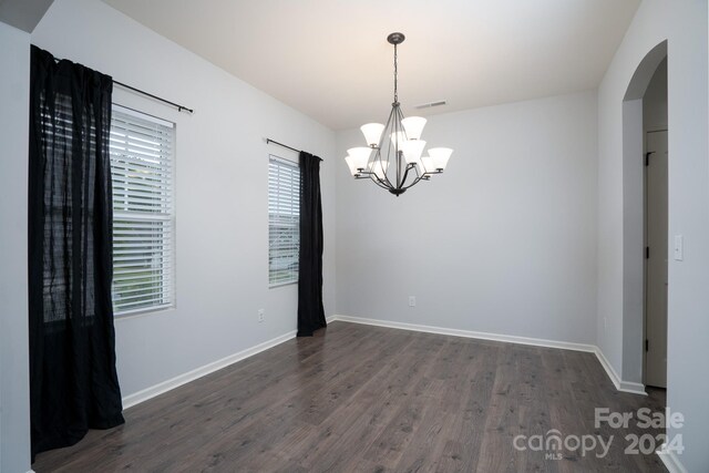 spare room featuring a notable chandelier and dark wood-type flooring