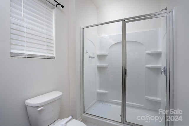 bathroom with a shower with shower door and toilet