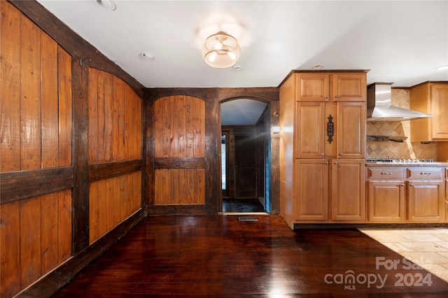 kitchen featuring wood walls, tasteful backsplash, wall chimney exhaust hood, dark wood-type flooring, and stainless steel gas stovetop