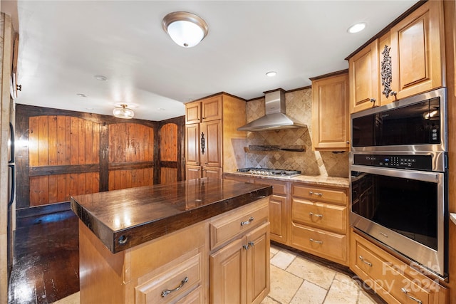 kitchen featuring dark stone counters, a center island, wall chimney exhaust hood, decorative backsplash, and appliances with stainless steel finishes