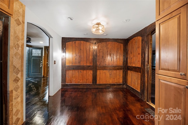 corridor featuring wooden walls and dark wood-type flooring