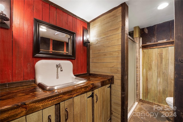 bathroom featuring vanity, wooden walls, toilet, and an enclosed shower